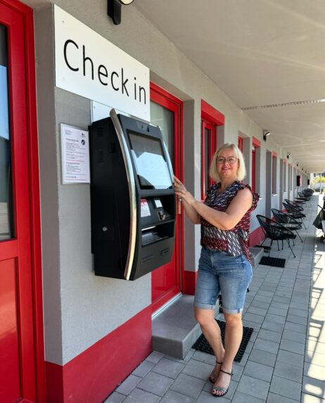 Sunny Hotel Regenstauf Nina Rudi am Self-Check-in-Terminal des Sunny Hotel Regenstauf vor Gästezimmern mit rotem Eingang